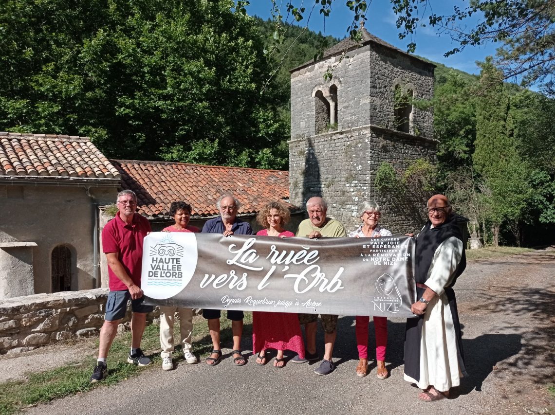 L'équipe des Compagnons du Sens et Frère Marie-Pâques présentant la banderole « La ruée vers l'Orb », initiative de promotion des vins et du patrimoine du territoire. Membres de l'association et Frère Marie-Pâques brandissant la banderole « La ruée vers l'Orb » devant la chapelle de Nize.