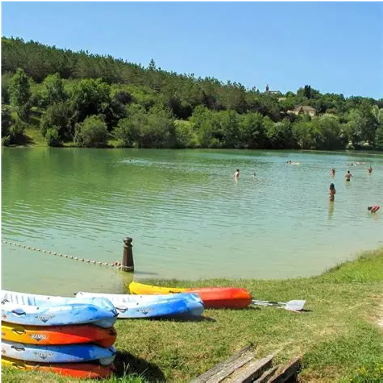 Activités nautiques et baignade sur le lac de 10 hectares de la base de loisirs de Molières. Kayaks colorés entreposés sur l'herbe au bord de l'eau avec des personnes qui se baignent dans le lac.