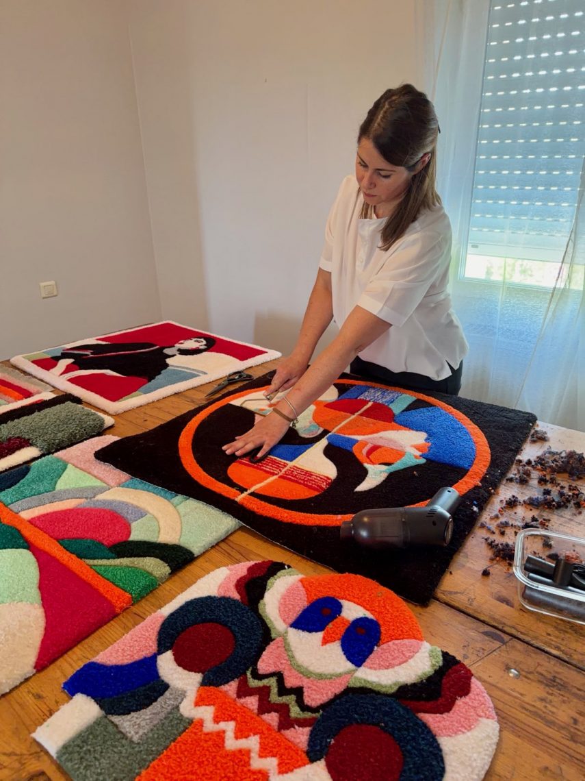 Audrey Guiraud en plein travail de finition méticuleux sur une œuvre en laine tuftée dans son atelier à Arvieu. Audrey Guiraud penchée sur une grande table en bois, égalisant au ciseau la surface d'un panneau artistique en laine tuftée aux motifs colorés.